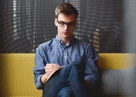 Person in Blue Denim Jacket Sitting on Chair While Writing